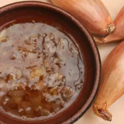 Un bol de sauce échalote, onctueuse et dorée, aux côtés de quelques échalotes fraîches.