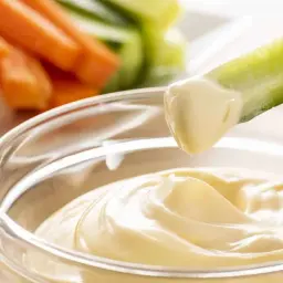Un bâtonnet de concombre est trempé dans une sauce onctueuse, parfaite pour accompagner des légumes crus comme des carottes, une recette facile de sauce pour tremper légumes crus marmiton.