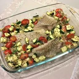 Filet de lieu noir au four avec tomates cerises et courgettes coupées en dés, assaisonné d'herbes.