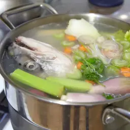 Une tête de poisson et des légumes mijotent dans une casserole, libérant un délicieux fumet de poisson.