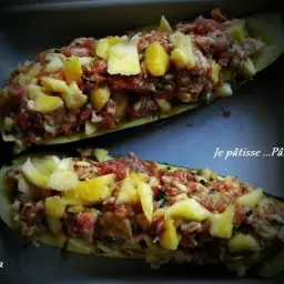 Deux courgettes farcies généreusement avec de la chair à saucisse et des morceaux de pommes de terre, prêtes à être cuites.