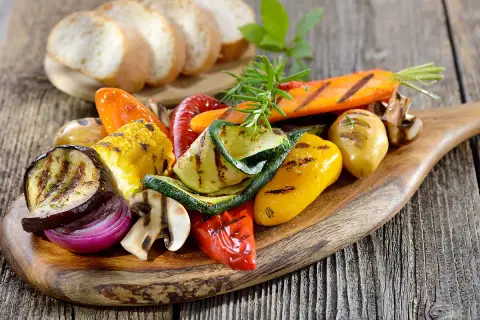 Légumes grillés colorés sur une planche en bois, accompagnés de pain frais. Un filet de crème de balsamique sublimerait ce plat.