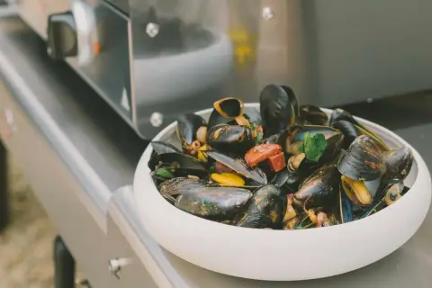 Un plat de moule plancha, garni de persil et de morceaux de chorizo, prêt à être dégusté.