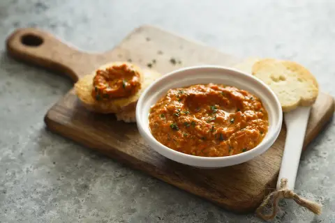 Un bol de poivronade, une recette méditerranéenne savoureuse, servi avec des toasts sur une planche en bois.