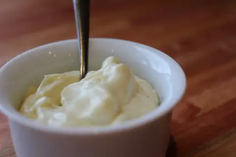 Une cuillère est plantée dans un bol de mayonnaise crémeuse, prête à être dégustée.