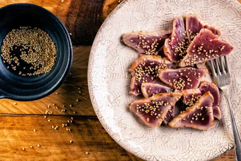 Tataki de thon, finement tranché et parsemé de graines de sésame, prêt à être dégusté. Une assiette élégante sur fond de bois rustique.