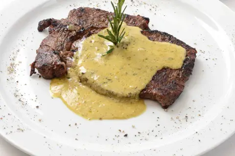 Un steak grillé, nappé d'une sauce crémeuse et garni d'une branche de romarin. Parfait pour accompagner une sauce pour entrecôte au barbecue.