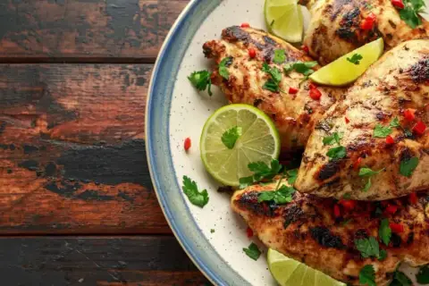Poulet grillé, garni de coriandre fraîche, de piment rouge et de quartiers de citron vert, évoquant une savoureuse marinade mexicaine.