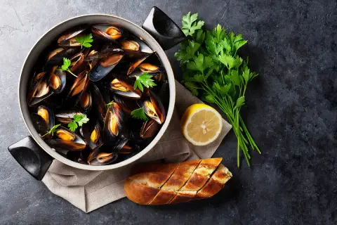Un plat de moules grillées, garni de persil frais, d'un quartier de citron et d'une baguette à l'ail, prêt à être dégusté.