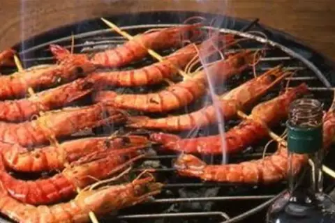 Gambas grillées sur un barbecue, fumantes et appétissantes. Une bouteille de sauce est à proximité, suggérant une délicieuse marinade pour gambas au barbecue.