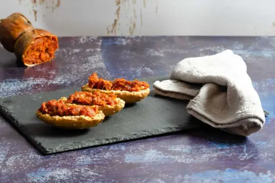 Tranches de pain garnies de sobrasada, un saucisson rouge épicé, avec un morceau de sobrasada entier en arrière-plan.