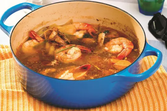 Une cocotte bleue contient une soupe de crevettes et de légumes, parfaite pour une sauce cocktail recette.