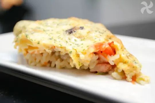Un plat unique convivial : riz, légumes et viande enveloppés dans une omelette dorée, saupoudrée d'herbes.