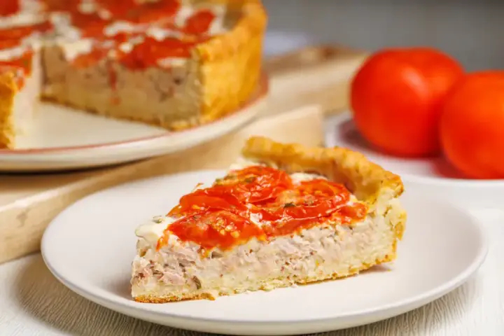 Une part de tarte au thon et tomates, garnie de tomates fraîches et d'une sauce crémeuse, prête à être dégustée.