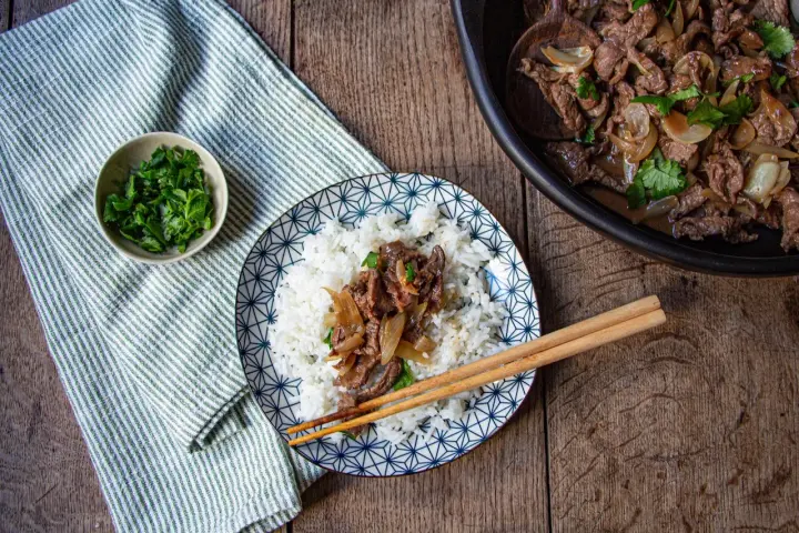 Un plat de riz blanc garni de boeuf aux oignons et de coriandre fraîche, prêt à être dégusté avec des baguettes.