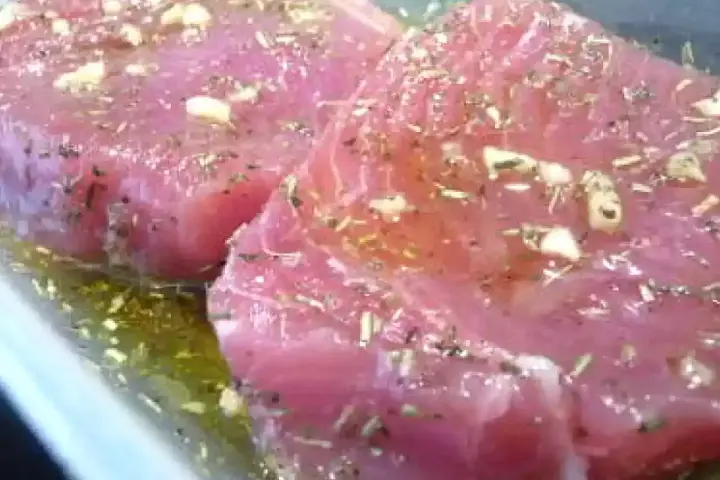 Deux beaux pavés de thon rouge marinés à l'ail et aux herbes, prêts pour une recette savoureuse.