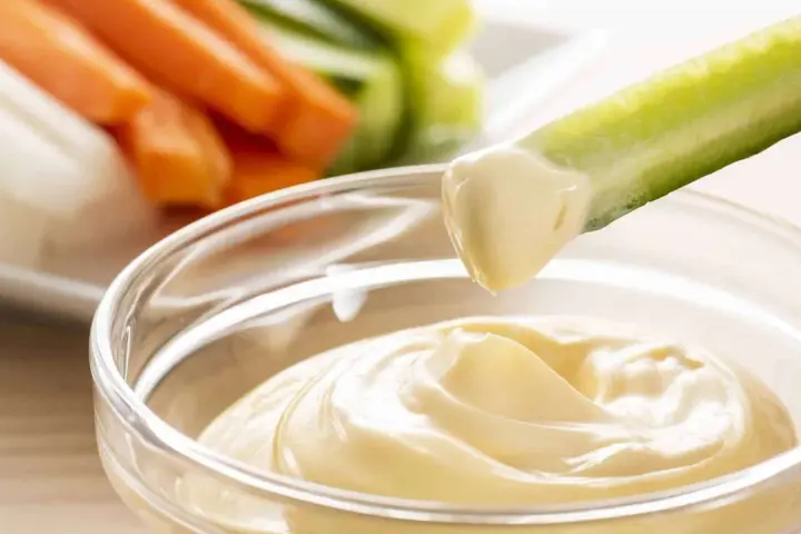 Un bâtonnet de concombre est trempé dans une sauce onctueuse, parfaite pour accompagner des légumes crus comme des carottes, une recette facile de sauce pour tremper légumes crus marmiton.