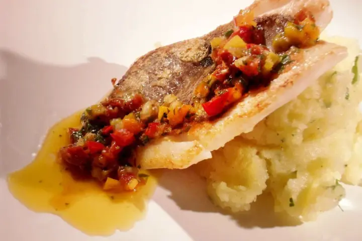 Filet de saint pierre poêlé, garni d'une concassée de légumes colorée, servi avec une purée onctueuse et un filet de sauce.