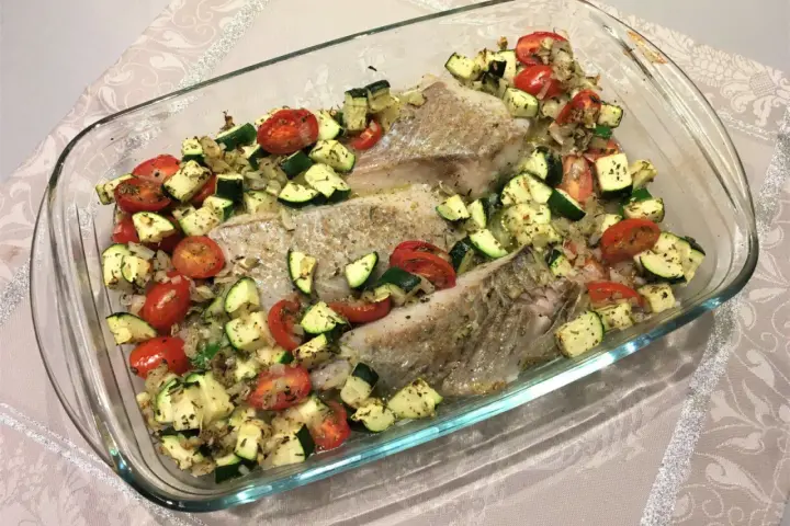 Filet de lieu noir au four avec tomates cerises et courgettes coupées en dés, assaisonné d'herbes.