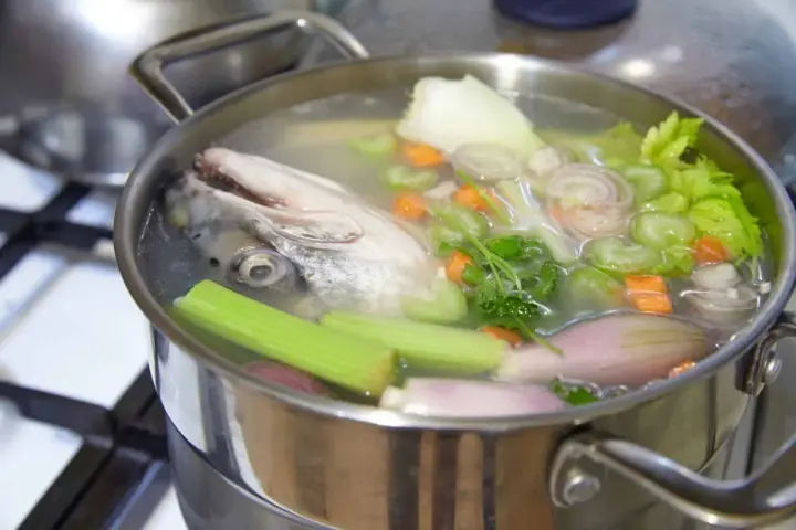 Une tête de poisson et des légumes mijotent dans une casserole, libérant un délicieux fumet de poisson.
