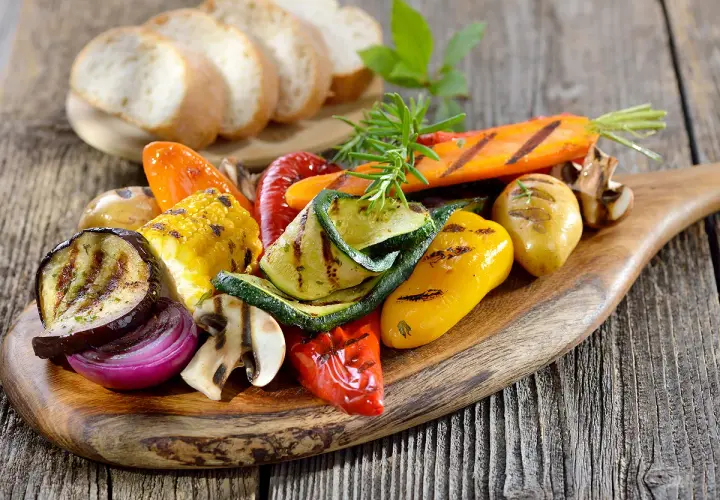 Légumes grillés colorés sur une planche en bois, accompagnés de pain frais. Un filet de crème de balsamique sublimerait ce plat.