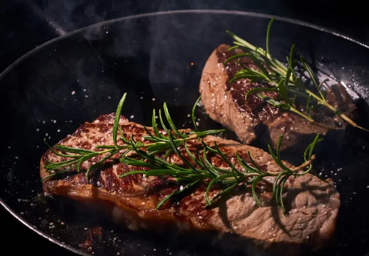 Deux steaks de boeuf Black Angus savoureux, poêlés avec du romarin et du gros sel, dégageant une vapeur alléchante.