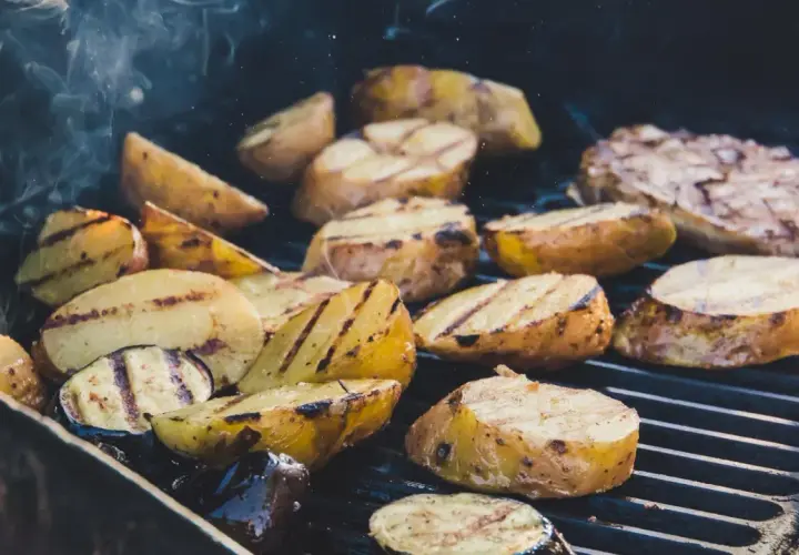 Pommes de terre coupées en quartiers, grillées à la perfection sur un barbecue, dégageant une fumée alléchante. Quelle pomme de terre barbecue !