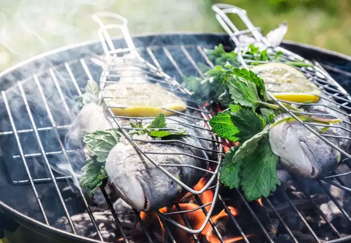 Deux poissons entiers sur un barbecue au charbon, garnis de citron et d'herbes fraîches, fumant doucement. Quel poisson au barbecue charbon !