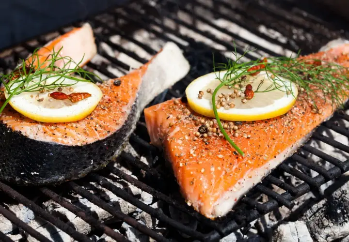 Deux pavés de saumon au barbecue, assaisonnés et garnis de citron et d'aneth, cuisent sur une grille chaude.