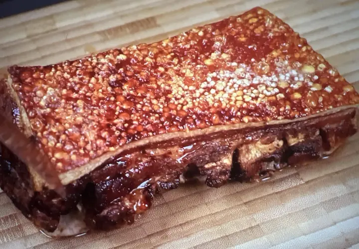 Poitrine de porc barbecue croustillante, avec une couenne dorée et des côtes apparentes, prête à être dégustée sur une planche en bois.