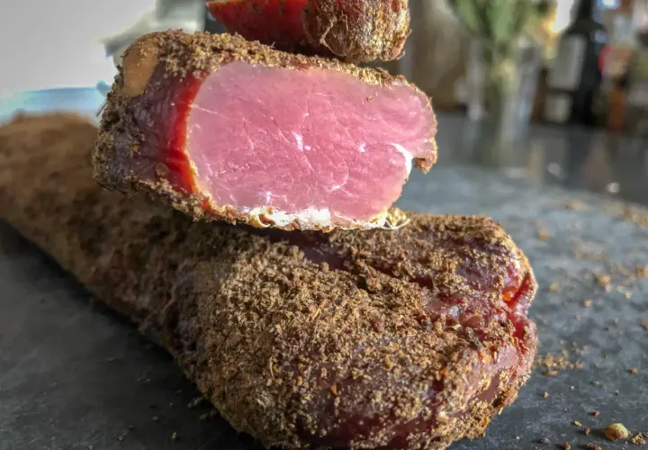 Un morceau de viande séchée, enrobé d'épices, dégage une odeur délicatement boucanée. Sa chair rose vif contraste avec sa croûte brune.