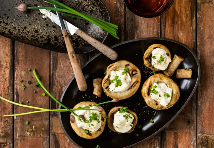 Champignons au barbecue farcis de fromage crémeux et garnis de ciboule fraîche. Un délice simple pour un repas estival.