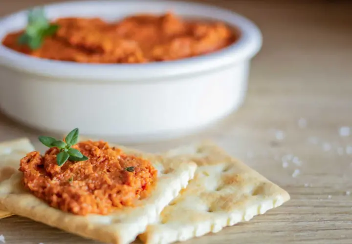 Une cuillère de rillette de chorizo, garnie d'une feuille de persil, sur des crackers. Un bol de cette délicieuse préparation est en arrière-plan.
