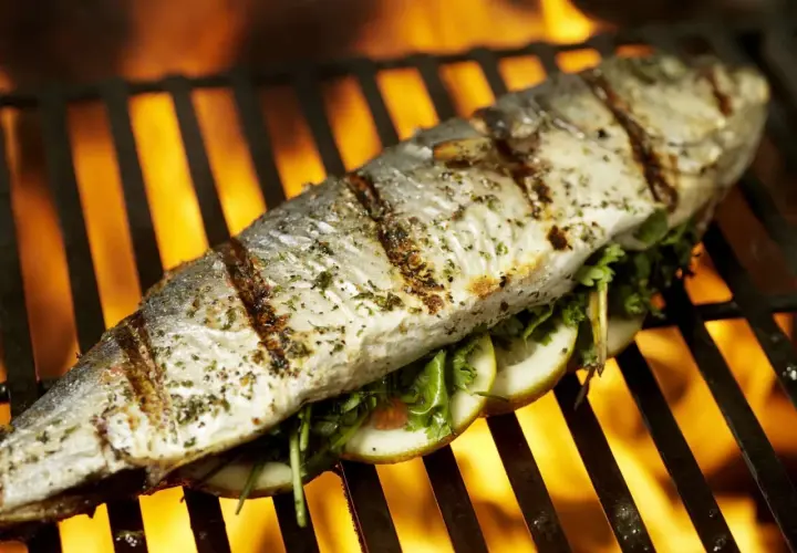 Poisson entier assaisonné, garni de tranches de citron et d'herbes, cuisant sur un gril avec des flammes vives en arrière-plan. Un délice de thon au barbecue.