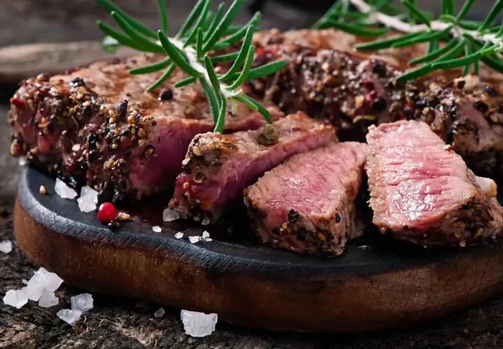 Un succulent filet mignon basse température, coupé en tranches, garni de romarin et de poivre concassé, sur une planche en bois rustique.