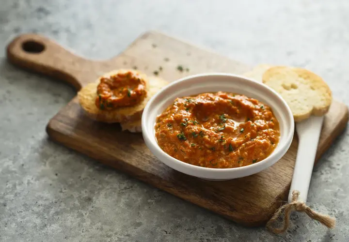 Un bol de poivronade, une recette méditerranéenne savoureuse, servi avec des toasts sur une planche en bois.