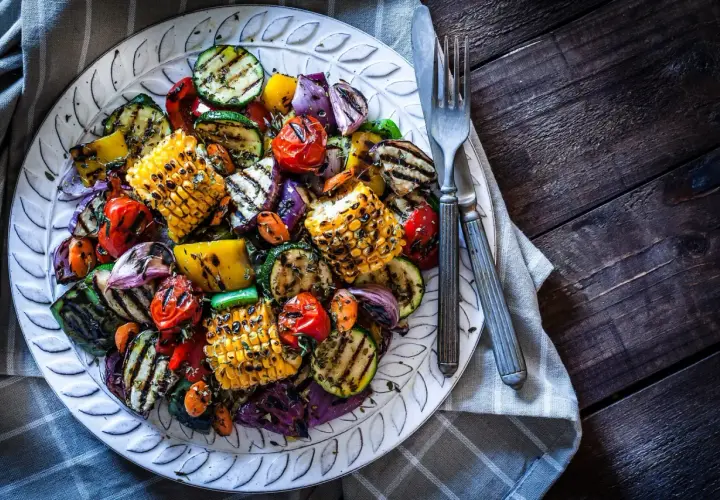 Assortiment coloré de légumes plancha : courgettes, maïs, poivrons, tomates cerises et oignons rouges grillés, assaisonnés d'herbes.