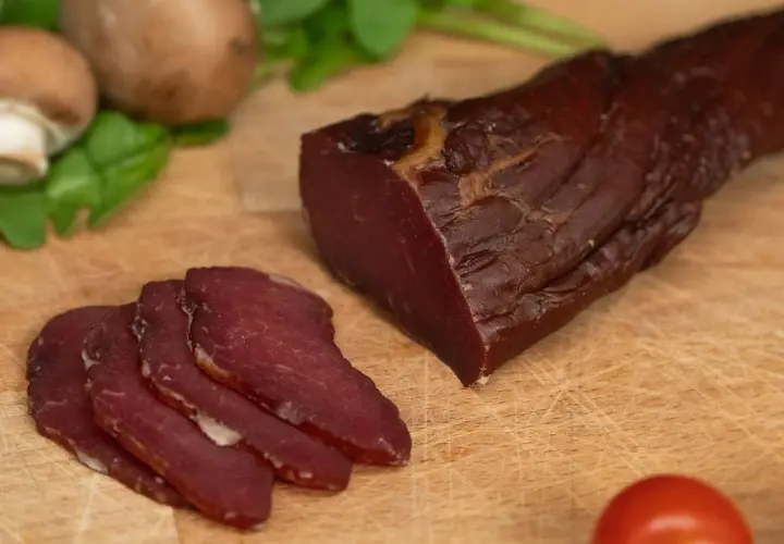 Filet mignon fumé, tranché, prêt pour le temps de fumage. Champignons et tomates en arrière-plan.