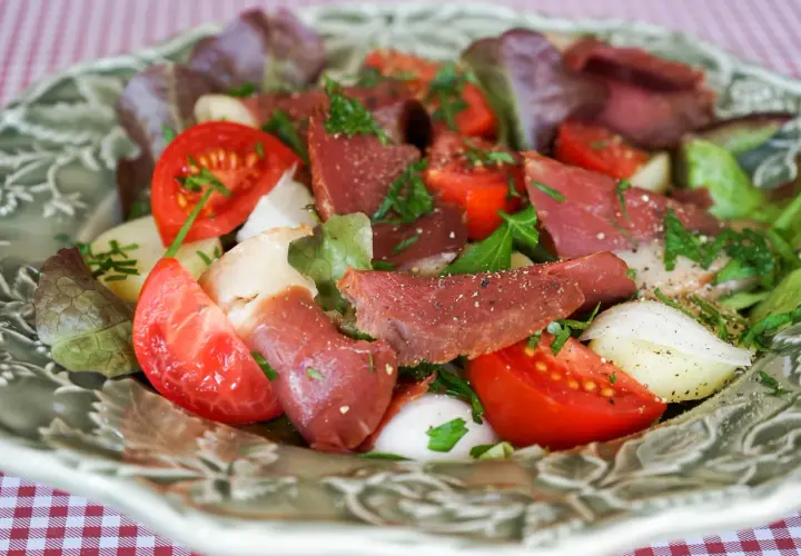Salade fraîche avec des tranches de fumer magret de canard, tomates, oignons et laitue, parsemée d'herbes.