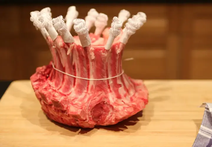 Une couronne d'agneau crue, prête pour la cuisson, avec les os protégés par du papier blanc.