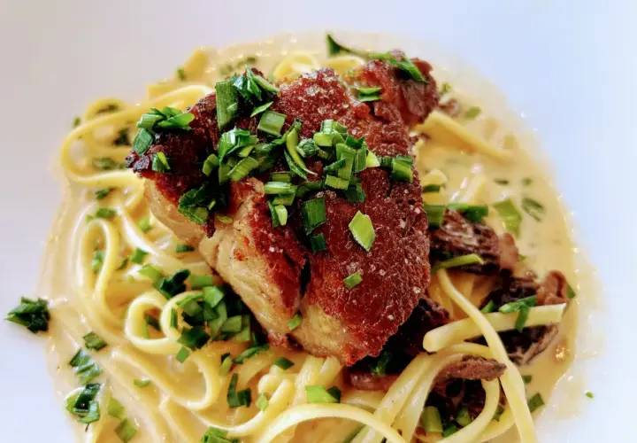 Un morceau d'échine de porc croustillante sur des pâtes crémeuses, garni de ciboule fraîche. Un délice !