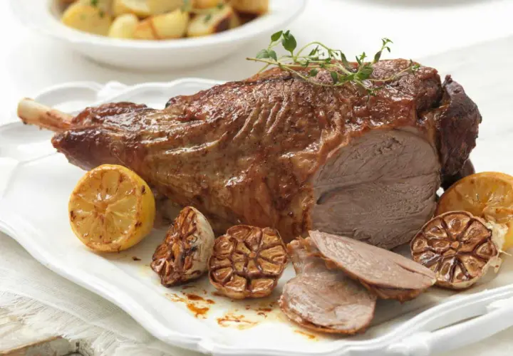 Gigot d'agneau rôti, parfumé au thym, servi avec des citrons grillés et de l'ail confit. Parfait pour une cuisson agneau barbecue réussie.
