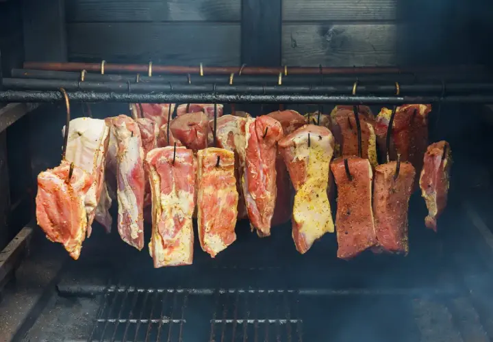 Viande crue assaisonnée suspendue dans un fumoir, prête pour le fumage. Le fumoir est alimenté par une bouteille de gaz.