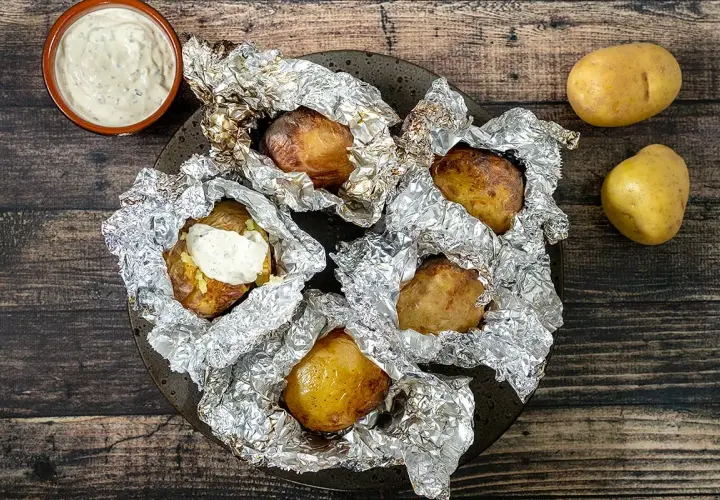 Pommes de terre en papillote sur barbecue, prêtes à être dégustées avec une sauce crémeuse. Le temps cuisson est parfait pour cette recette.
