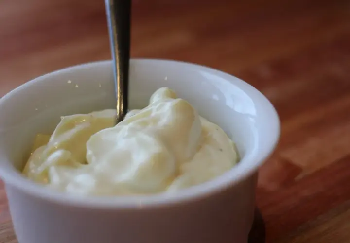 Une cuillère est plantée dans un bol de mayonnaise crémeuse, prête à être dégustée.