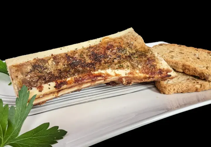 Un os à moelle rôti, assaisonné d'herbes et de poivre, servi avec des toasts croustillants sur une assiette blanche.