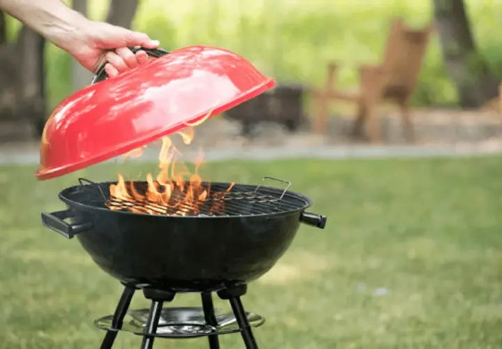 Maintenant, apprenons comment éteindre un barbecue. Une main soulève le couvercle rouge d'un barbecue noir où des flammes dansent.