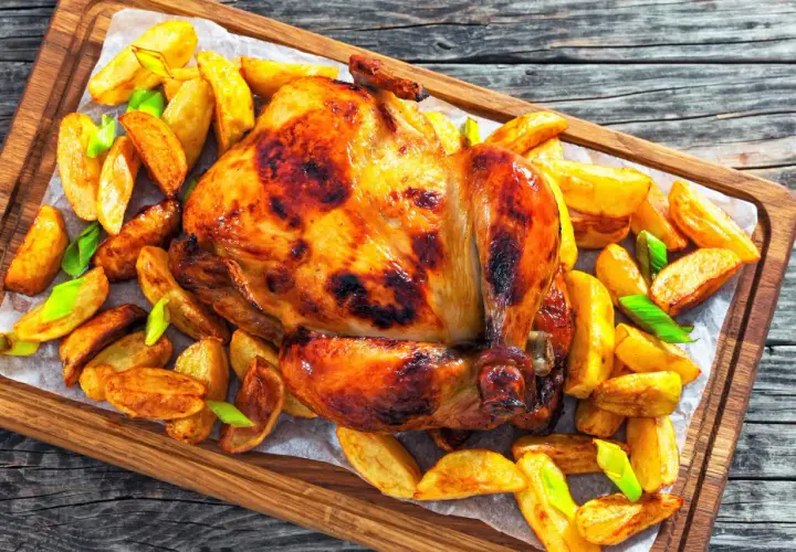 Un poulet rôti doré et croustillant, entouré de pommes de terre rôties et d'oignons verts, prêt à être dégusté.