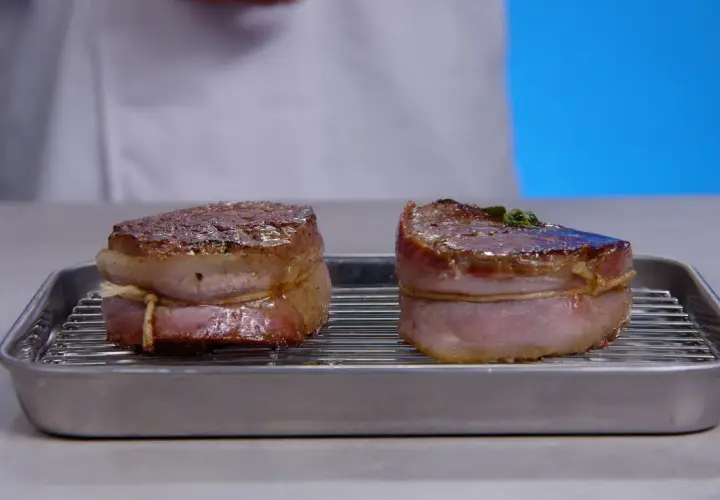 Deux filets mignons au barbecue, enveloppés de lard, reposent sur une grille dans un plat.