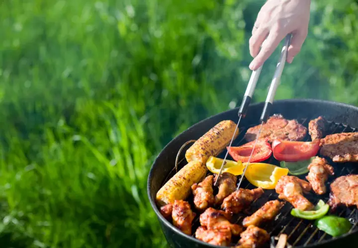 Un barbecue sain en plein air avec des épis de maïs, des poivrons colorés et des brochettes de poulet grillant sur le feu.
